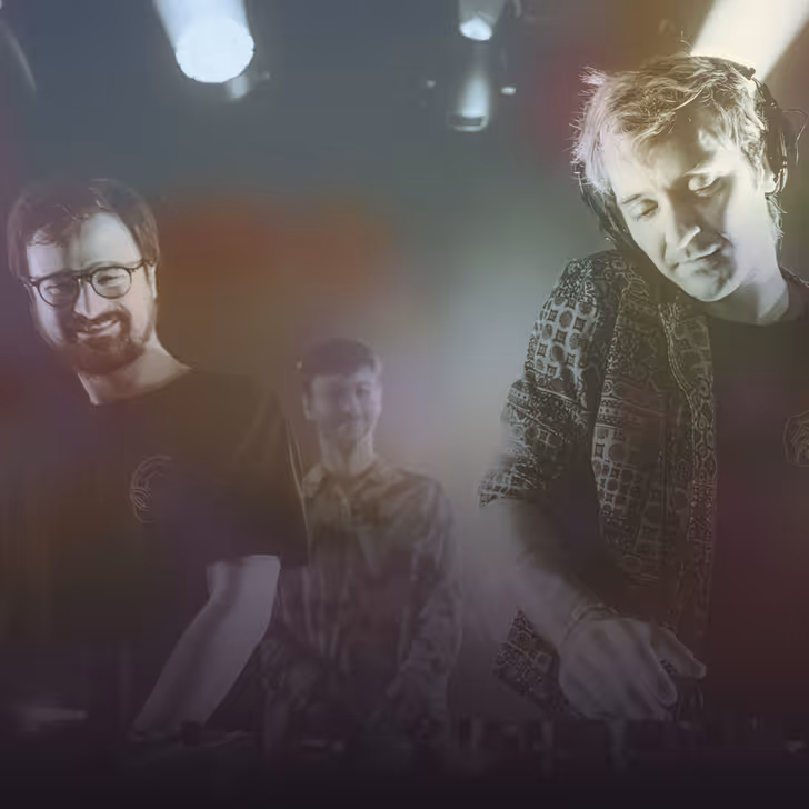 Trois DJs souriants concentrés sur leurs platines sous des lumières de scène tamisées.