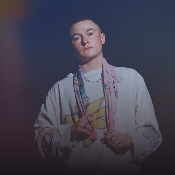 Personne avec une écharpe rose et un sweat-shirt blanc portant des bijoux, regardant vers l'avant.