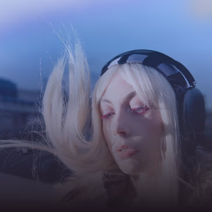 Jeune femme aux cheveux blonds flottants portant un casque audio noir avec fond bleu.