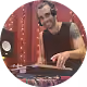 Un DJ en t-shirt noir en train de mixer sur une platine avec un micro près de lui.
