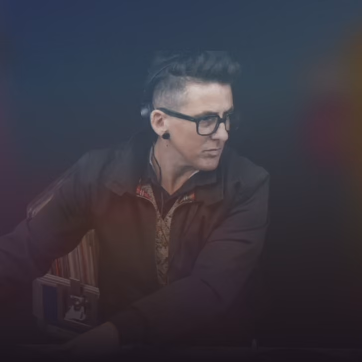 Homme portant des lunettes et une veste sombre, regardant vers la droite sur un fond flou.