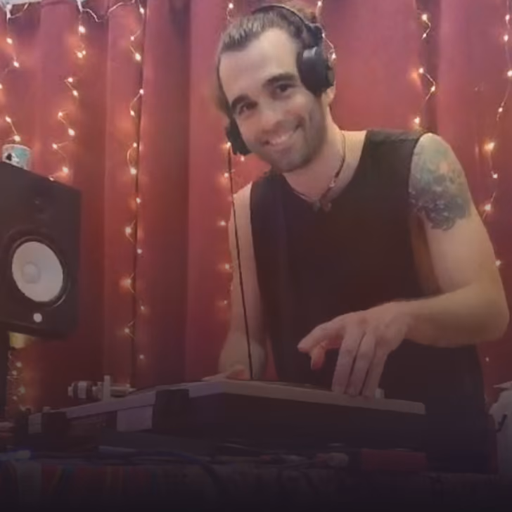 Un DJ souriant avec un tatouage à l'épaule, portant un casque, mixant de la musique en studio.