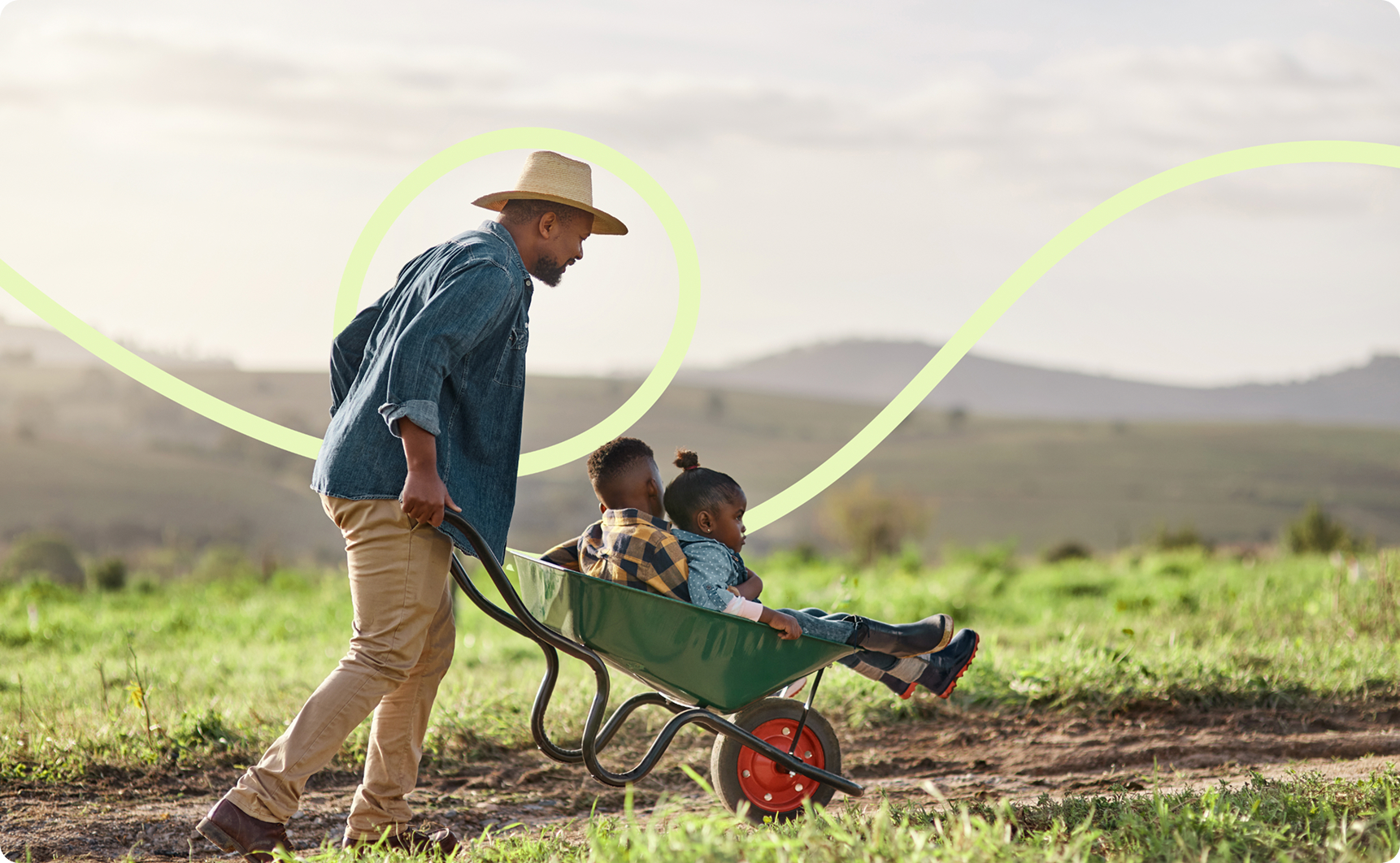 A man in the countryside with a wheelbarrow with children in it.