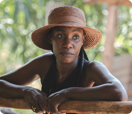 A woman with a hat leaning on a fence.