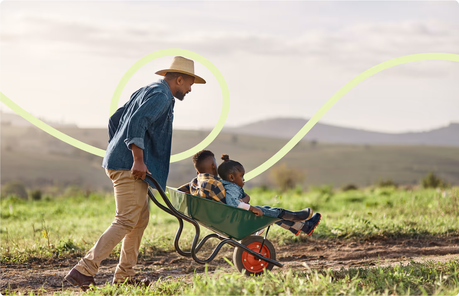 A man in the countryside with a wheelbarrow with children in it.