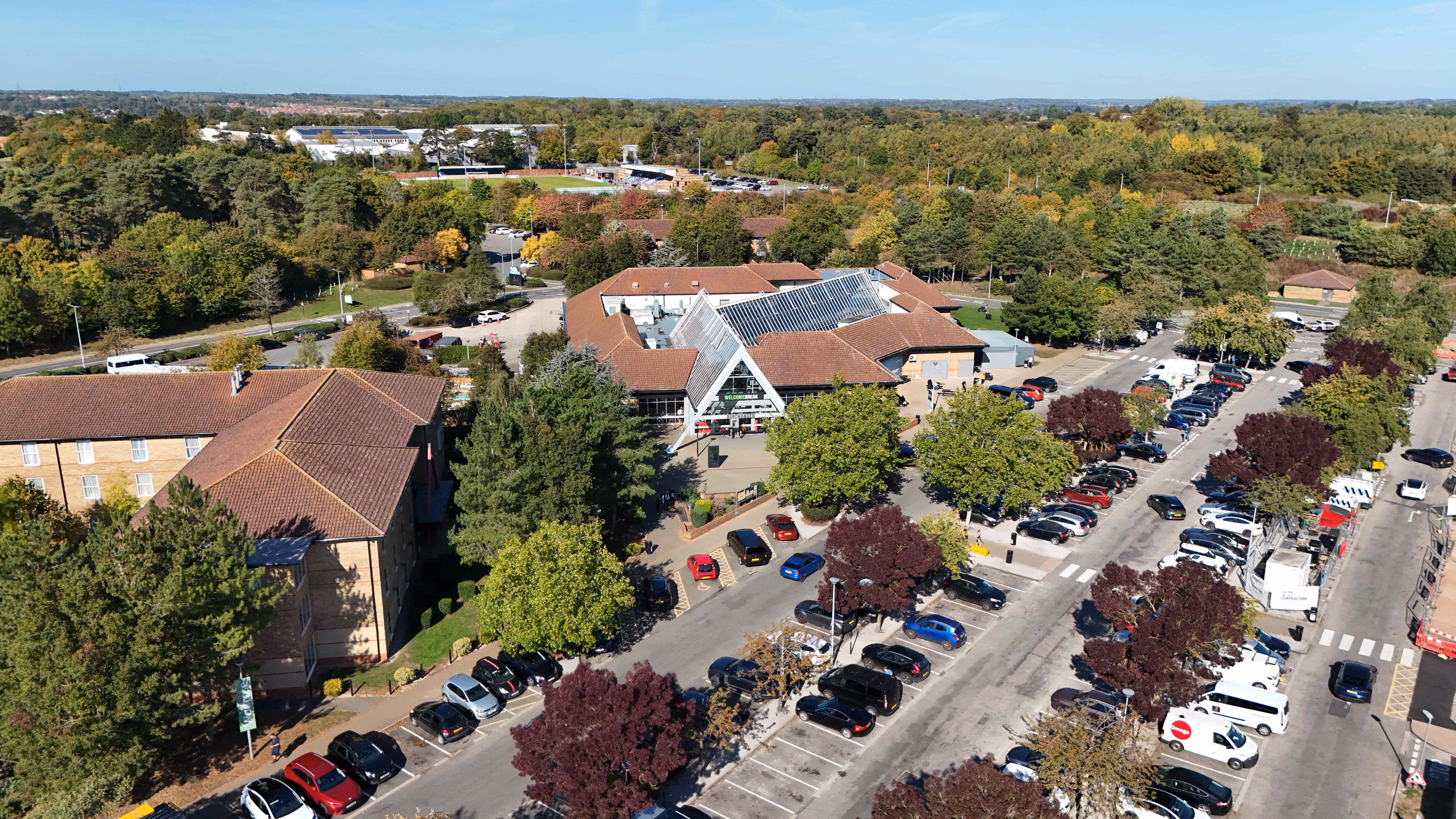 Aerial view of a Birchanger services surrounded by trees and a parking lot with cars.
