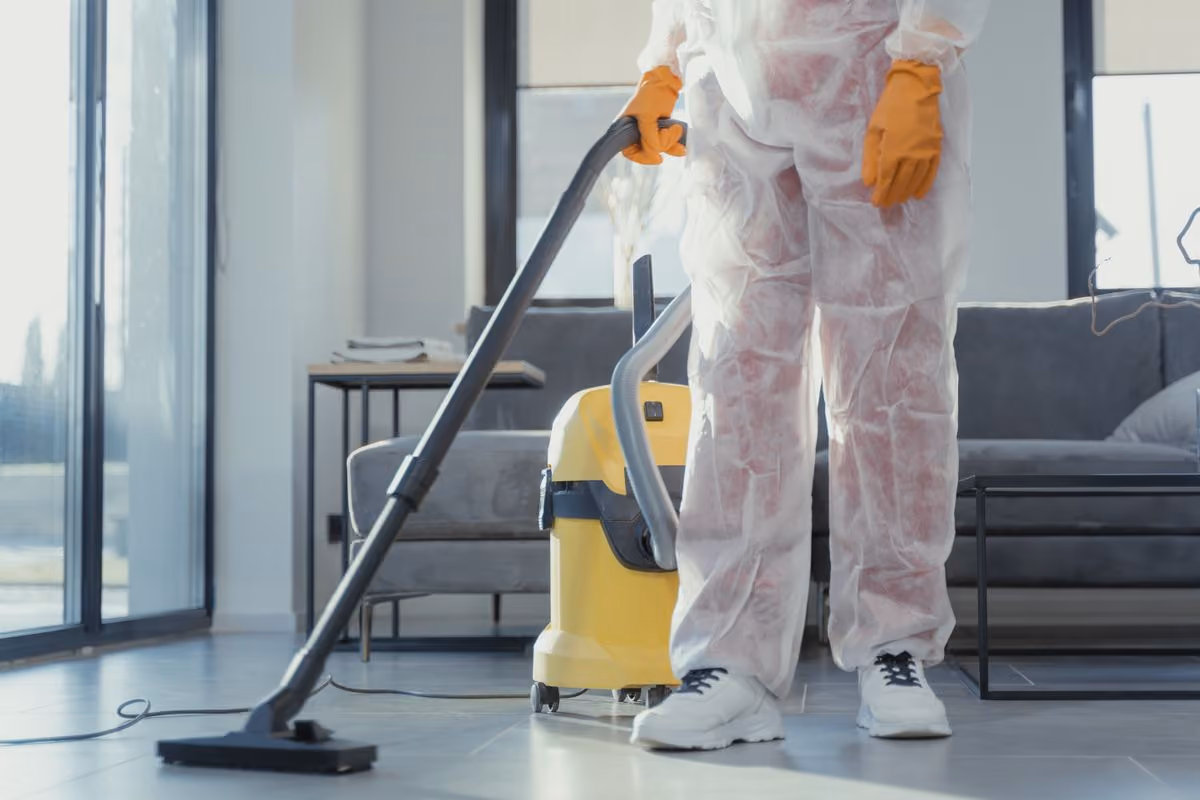 Reinigungskraft in Schutzkleidung saugt einen modernen Wohnraum