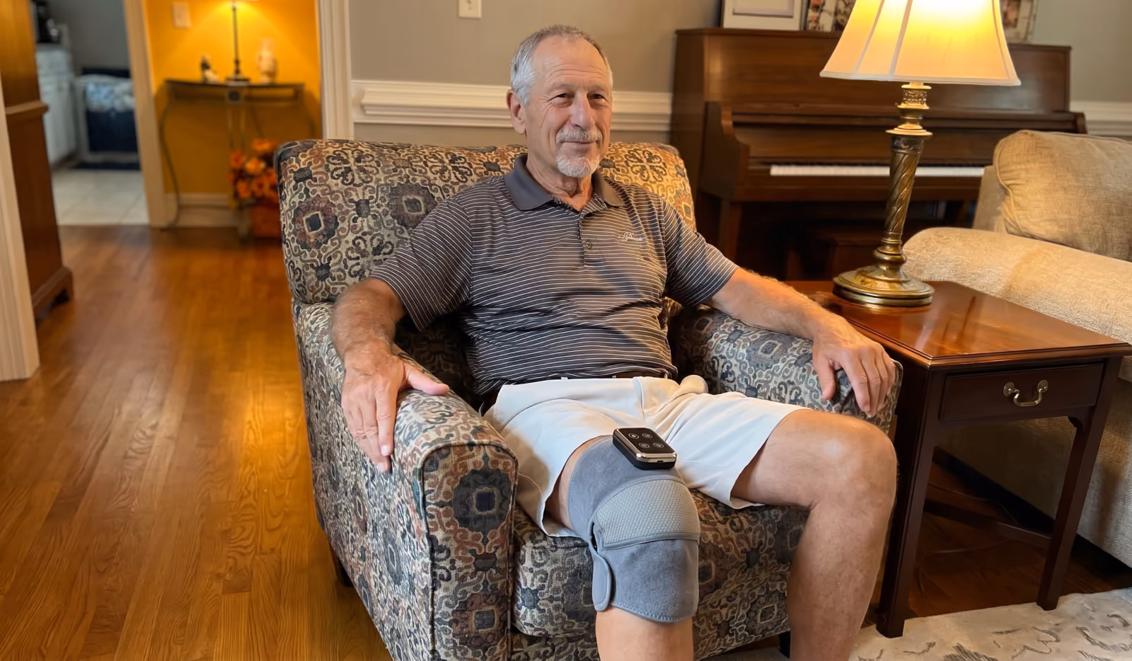 A man in his sixties sitting in a living-room armchair with the grey EMSense knee wrap fastened around his right knee