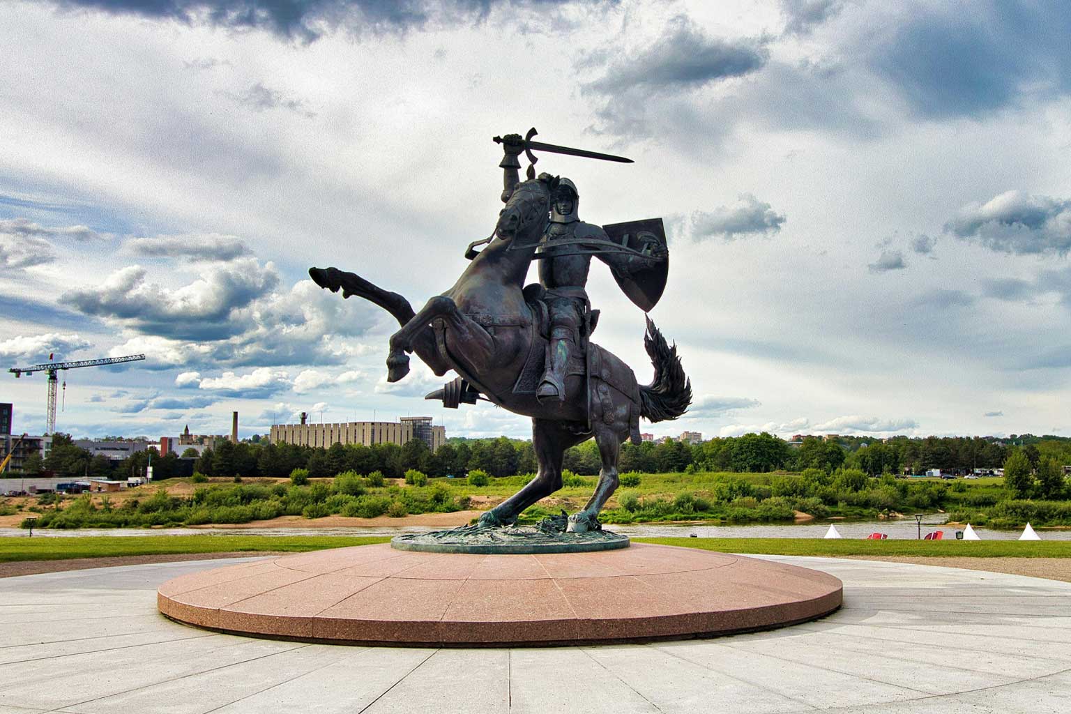 Large outdoor statue of a mounted warrior with a sword and shield, showing a protective coated metal surface against a dramatic sky and landscaped surroundings.