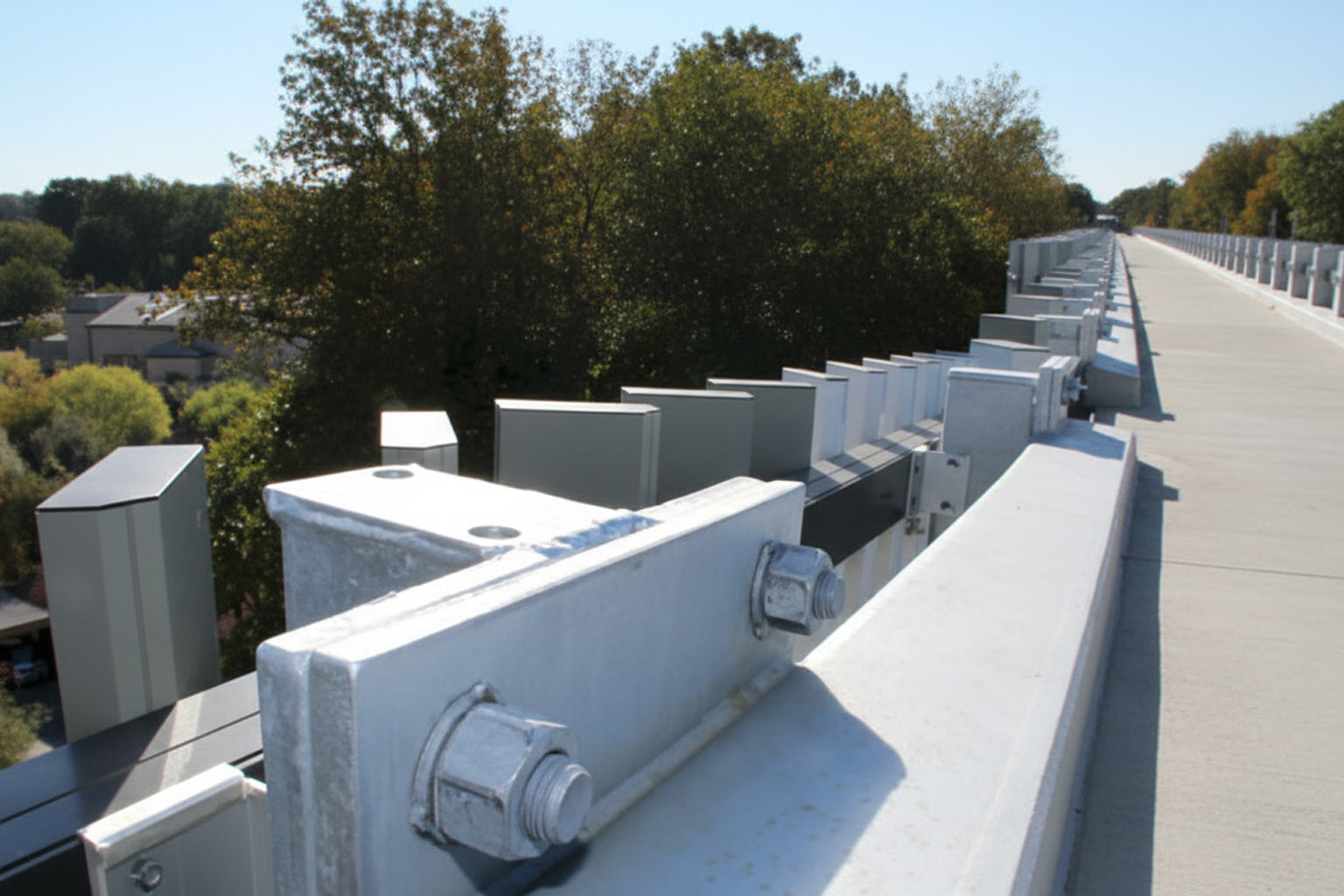 Close-up view of galvanized structural steel bridge connections featuring bolts, nuts, and railing components under bright outdoor lighting.