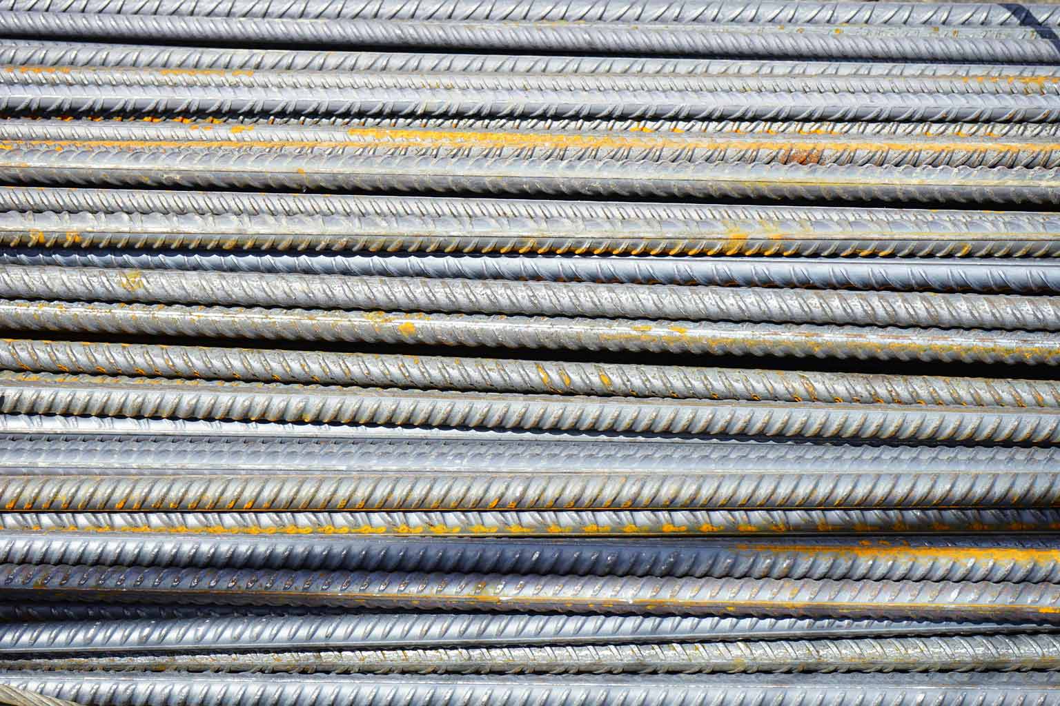 Close-up view of stacked galvanized reinforcing steel bars, showing ribbed texture and light surface oxidation across multiple layers.