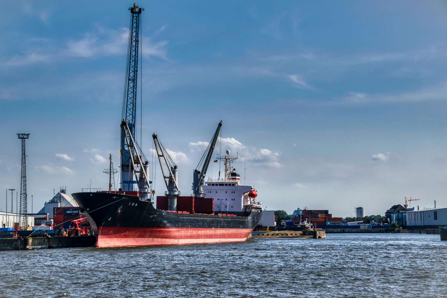 Cargo ship docked at an industrial port with cranes and shipping containers, illustrating marine exposure and corrosive water environments.