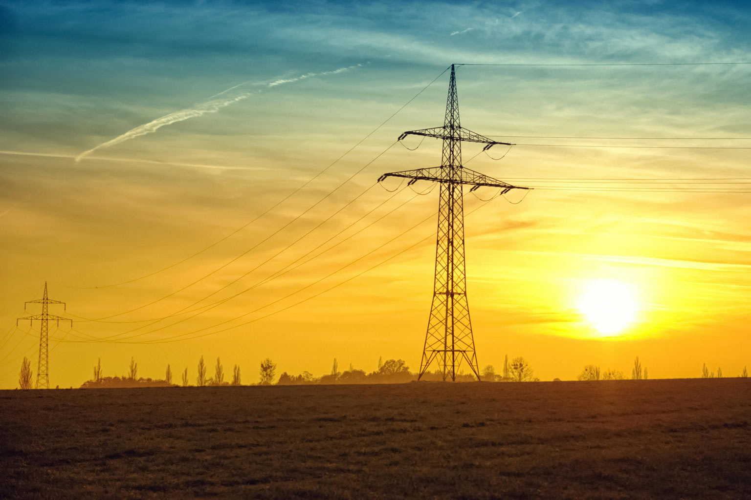 Electric transmission towers and power lines silhouetted against a sunset sky, highlighting atmospheric exposure conditions for utility structures.