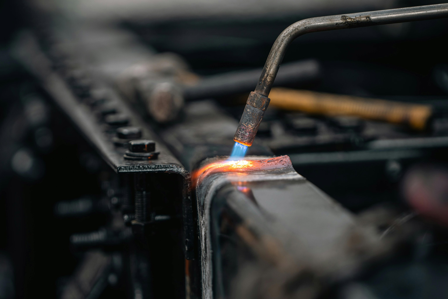 Close-up of a torch heating a galvanized steel joint, showcasing pre-weld preparation and metal heating during fabrication.