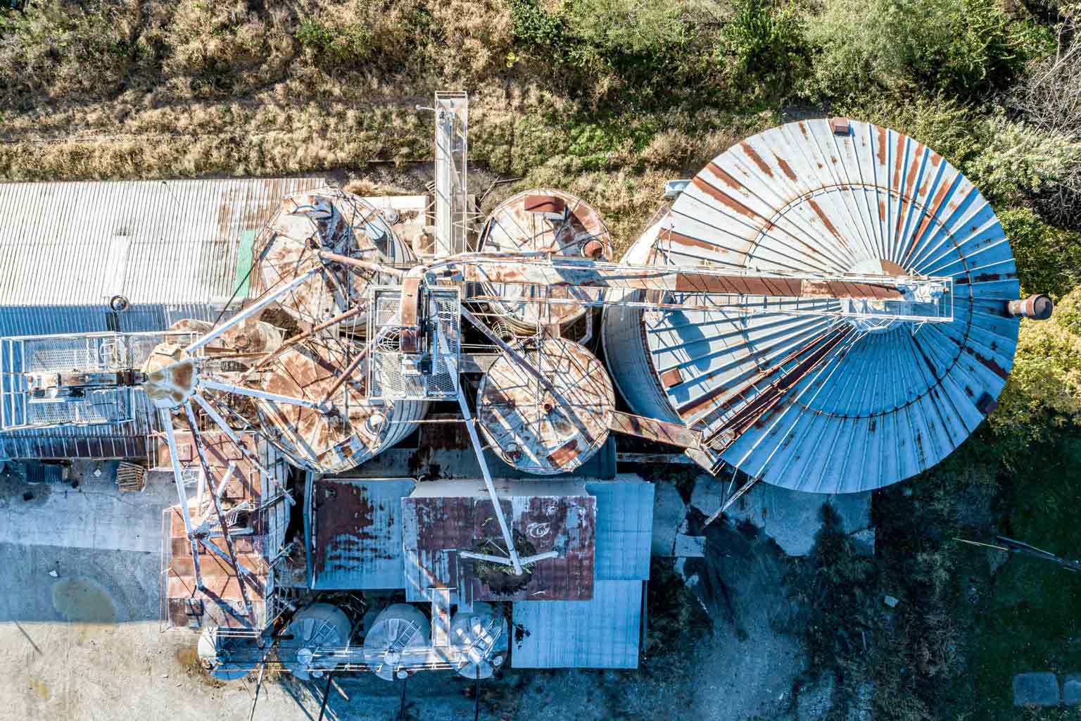 Top-down aerial view of an industrial site with rusted storage silos and metal structures, showing corrosion on exposed steel surfaces.