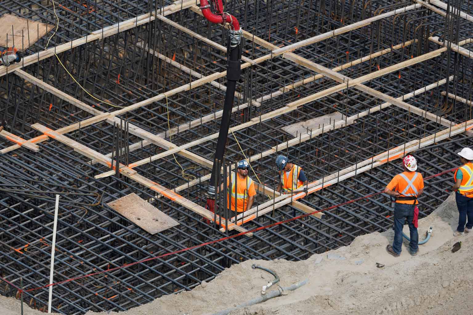 Construction crew standing inside a dense grid of reinforcing steel as concrete is placed, illustrating chromate-passivated galvanized rebar being embedded into a structural foundation.