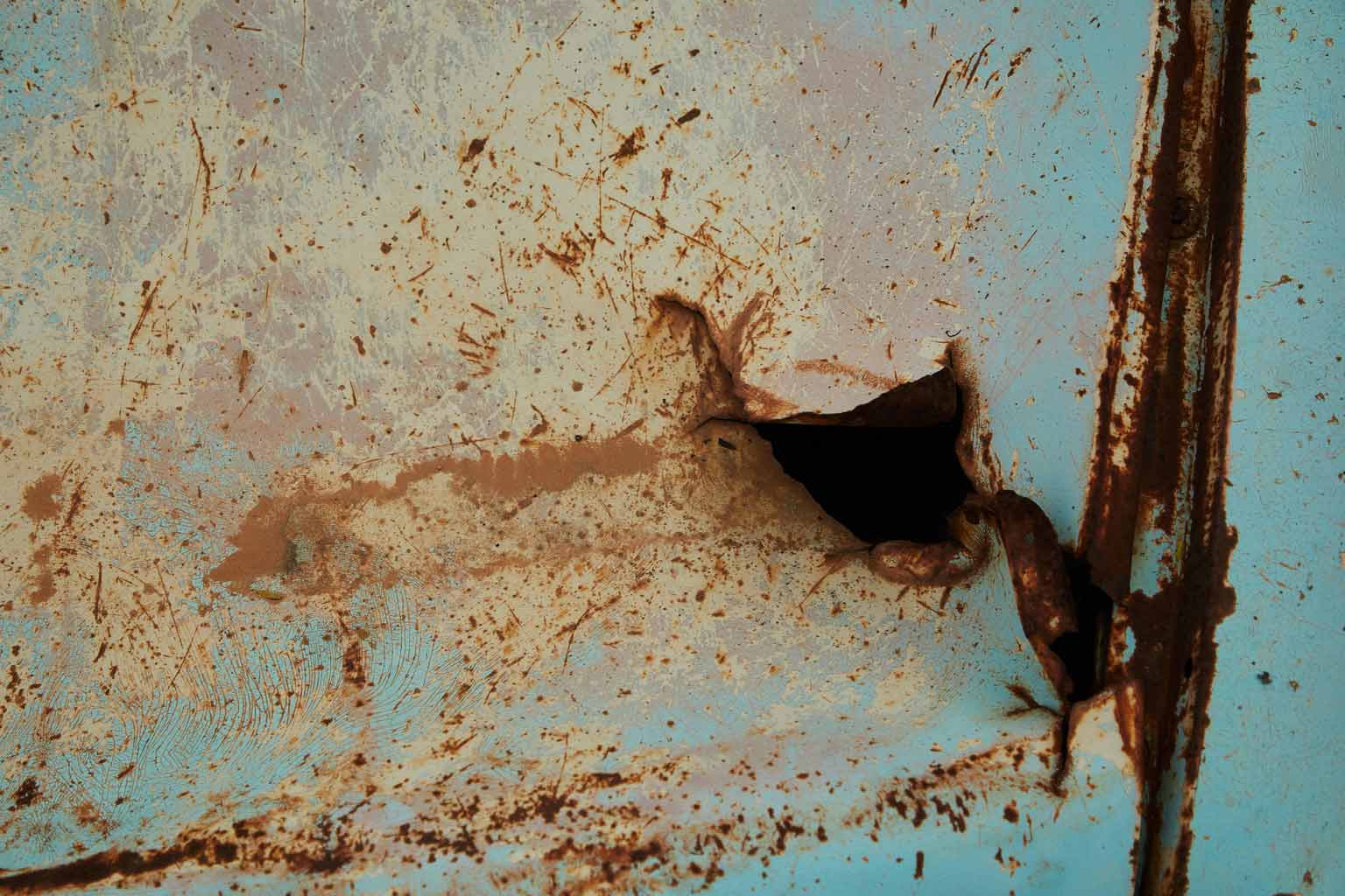 Severely corroded steel surface with a jagged hole and flaking paint, depicting the consequences of poor internal protection and the need for proper progressive dipping of poles.