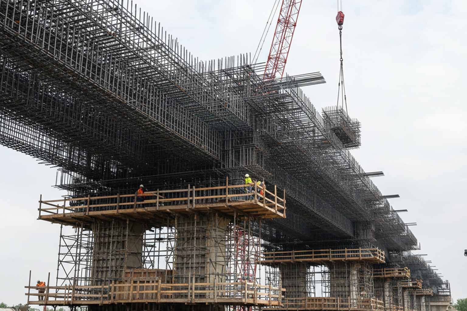 Massive bridge deck under construction with dense rebar cages and workers on scaffolding, representing long-term durability modeling for galvanized rebar in chloride-rich environments.