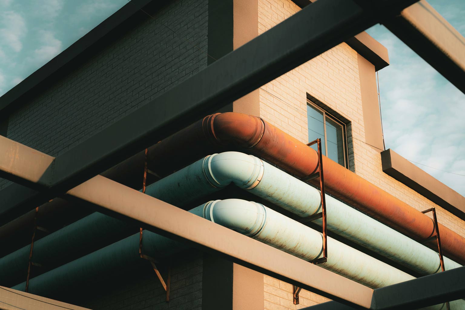 Industrial building with parallel exterior pipes, some rusted and others coated, symbolizing variability in protective coating performance and the need for statistical evaluation of thickness.
