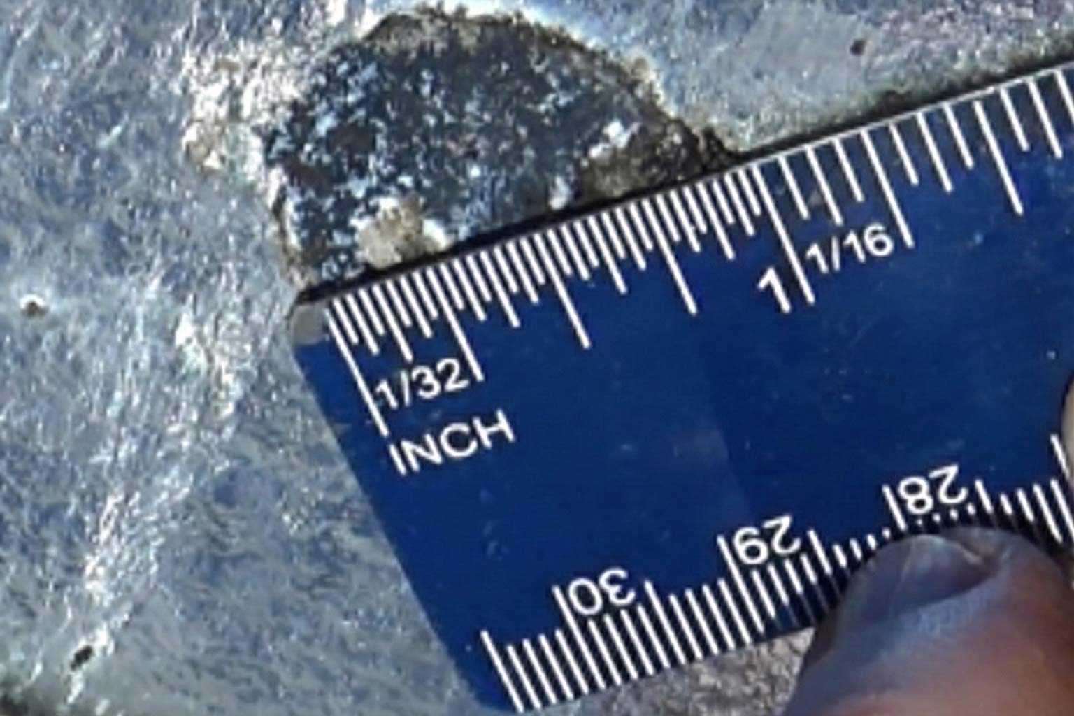 Close-up of a ruler measuring a damaged or bare spot on a galvanized steel surface to assess repair size requirements.