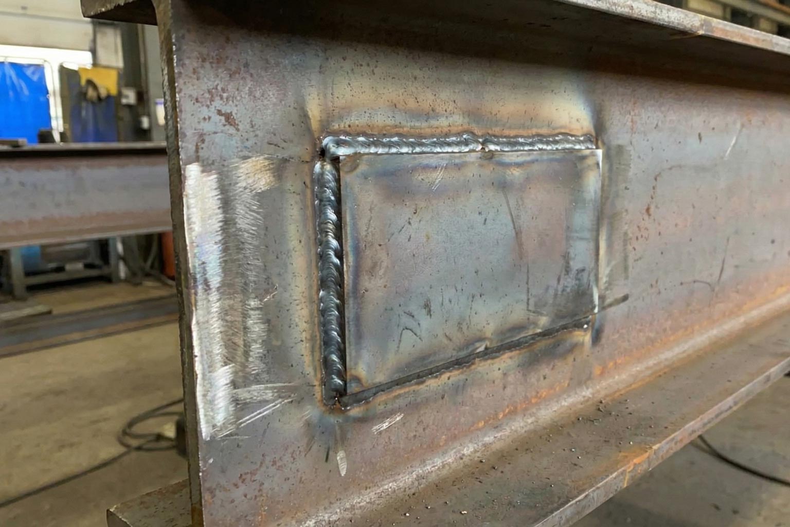 Close-up of a welded steel plate reinforcement on a structural beam, showing discoloration and heat-affected zones caused by fabrication prior to galvanizing.