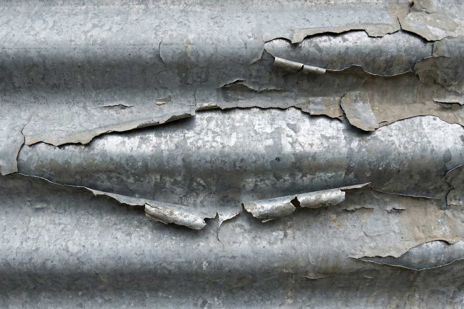 Close-up of severely peeling and flaking galvanized coating on corrugated steel, showing coating failure along thermally cut edges.