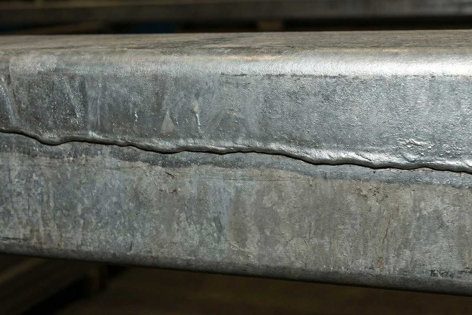 Galvanized structural steel beam with visible overlap line from progressive dipping, showing coating variation along the edge.