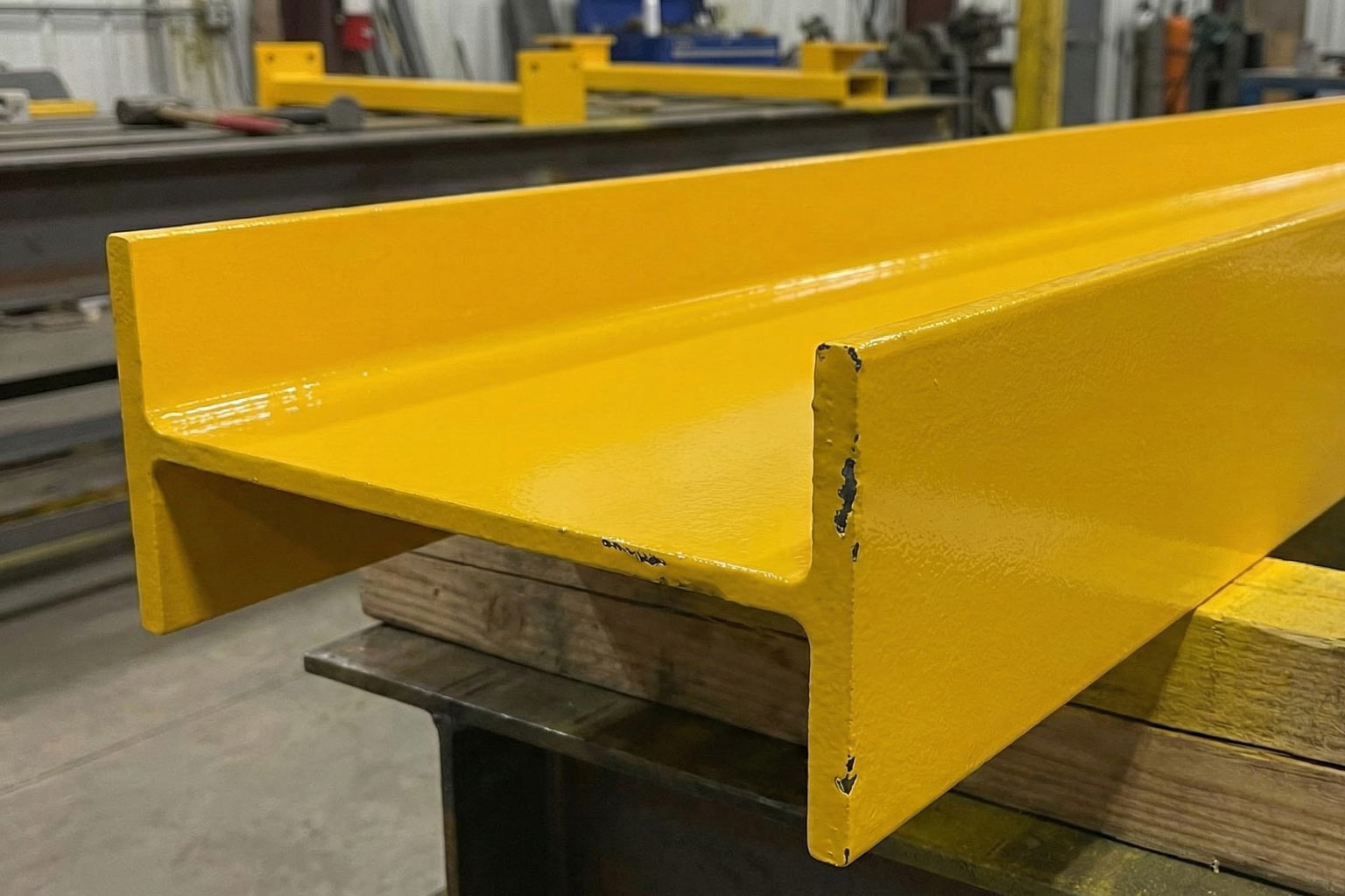 Yellow-painted structural steel channel with chipped coating at the edges, showing the importance of proper surface preparation before coating.