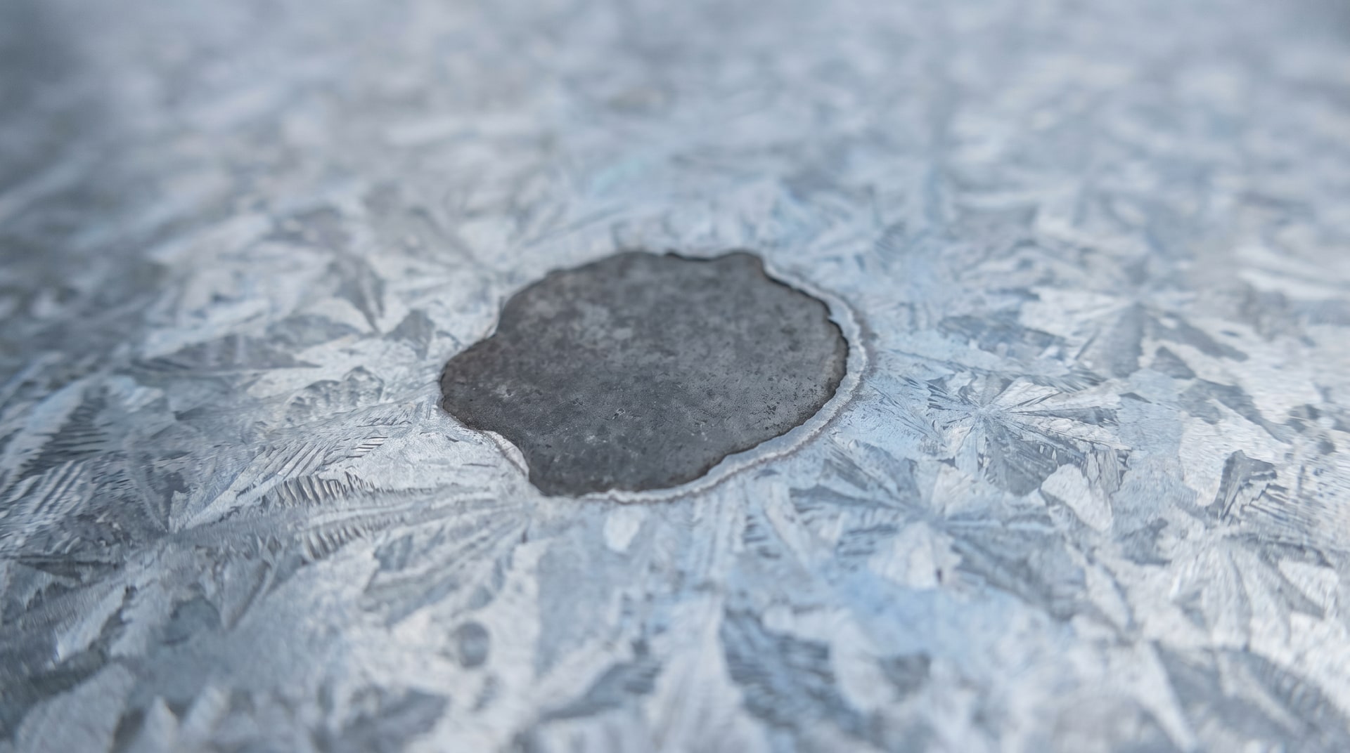 Small bare spot on galvanized steel surface showing exposed base metal