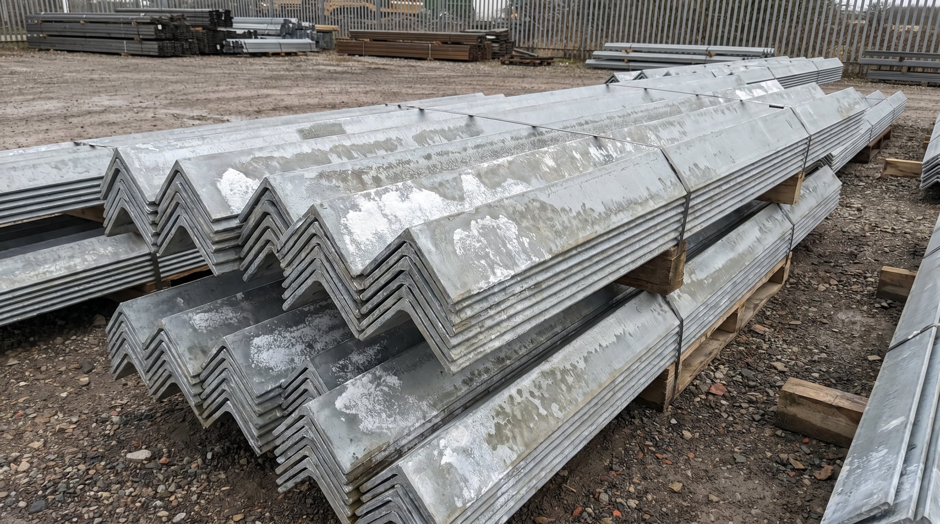 Stacks of newly galvanized steel angle iron showing white powdery wet storage stain deposits on zinc coating surfaces in an outdoor storage yard.