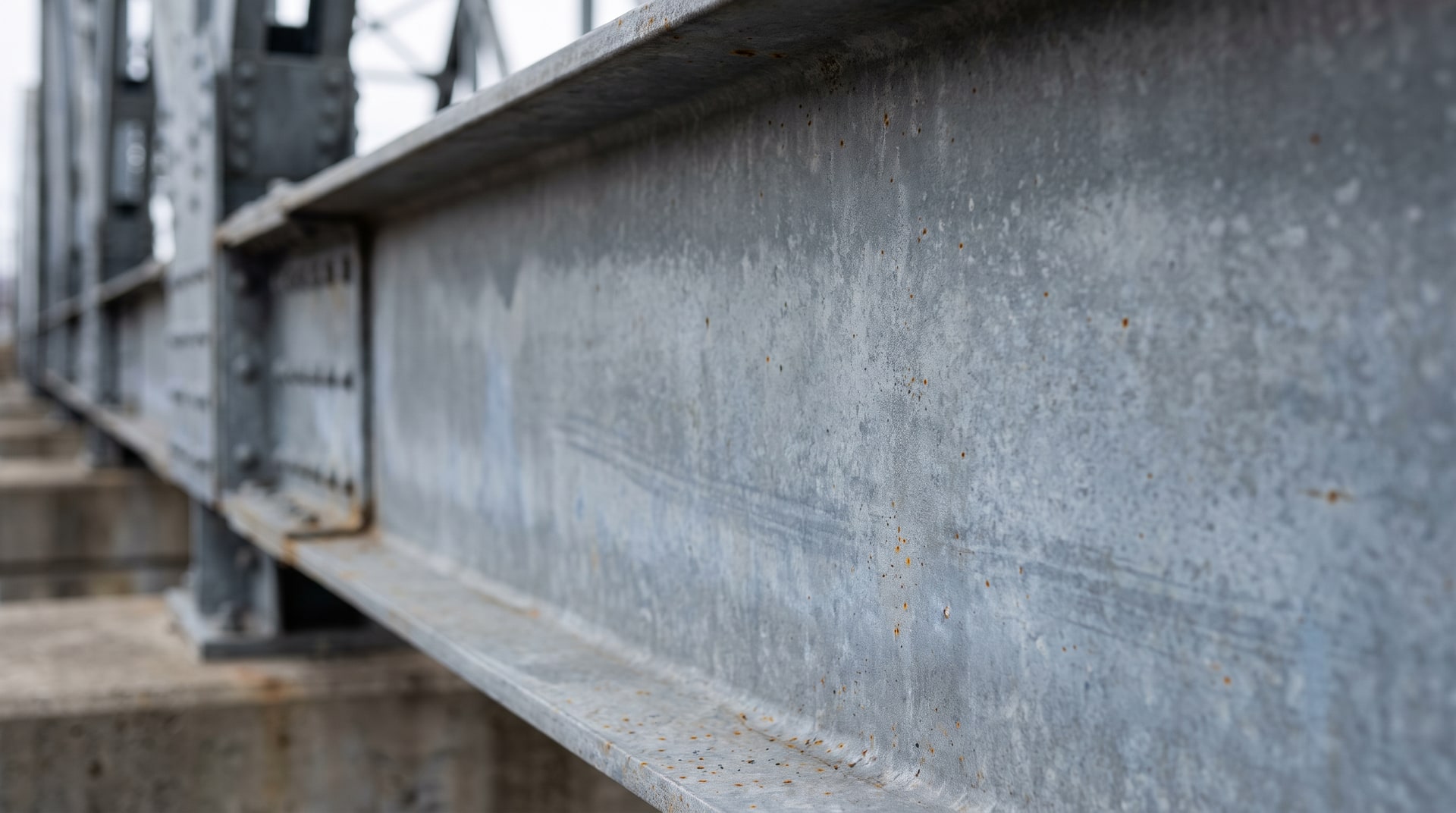 Close-up of a weathered hot-dip galvanized steel bridge beam showing a uniform matte gray zinc patina surface after ten years of outdoor exposure.