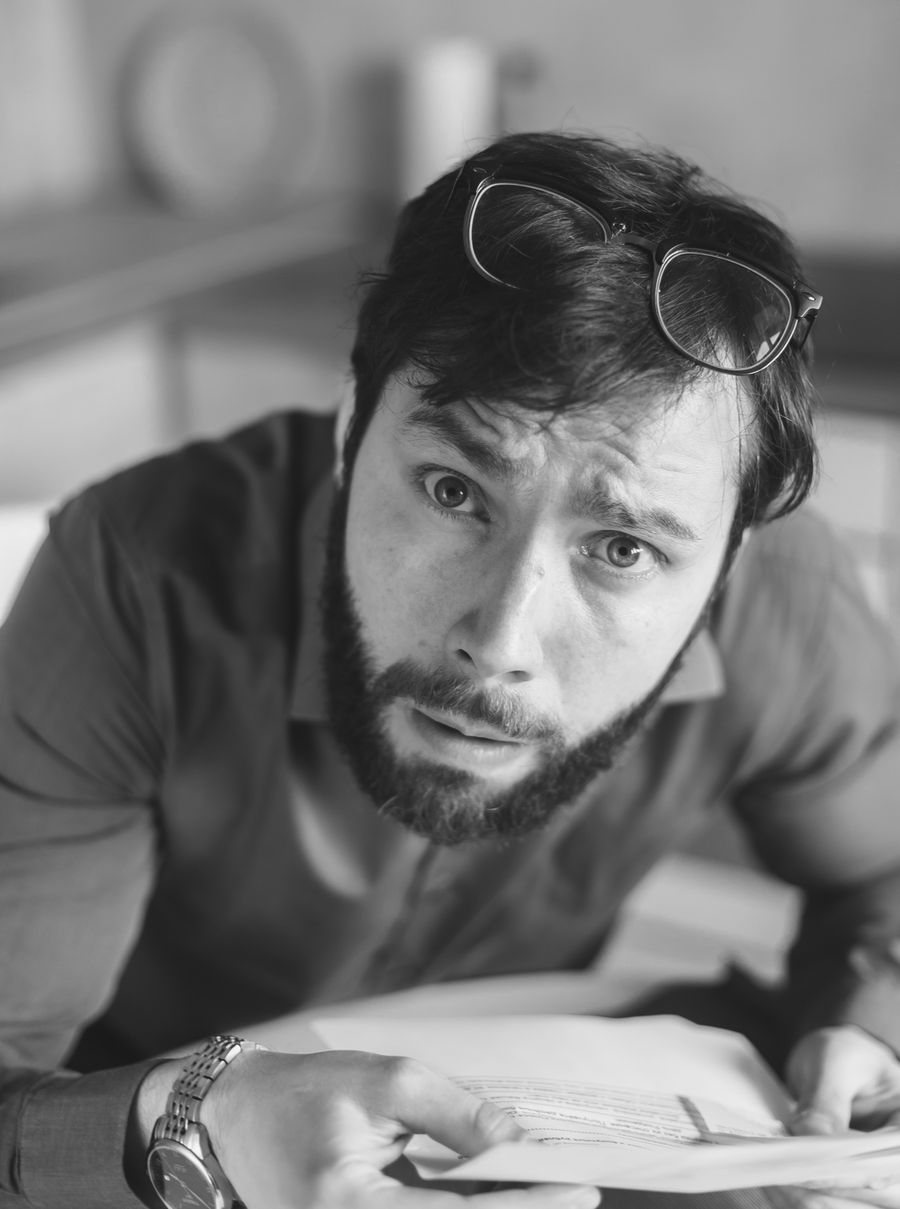 Black and white photo of a bearded man looking perplexed while holding papers