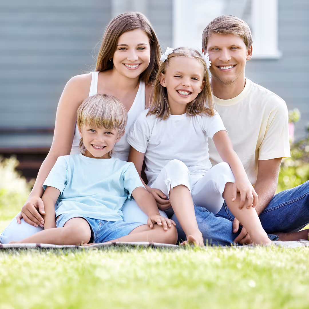 family with 2 small children smiling on front lawn