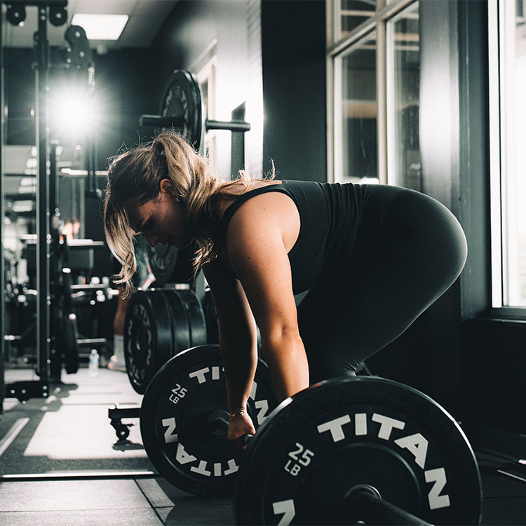 A woman leaning over to pick up a barbell at Elite Fit Labz