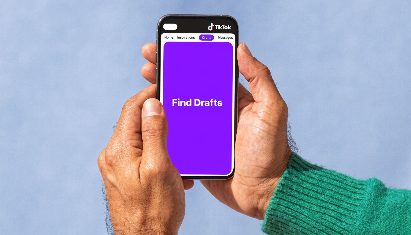 A person holding a smartphone displaying the TikTok app interface with a purple Find Drafts screen.