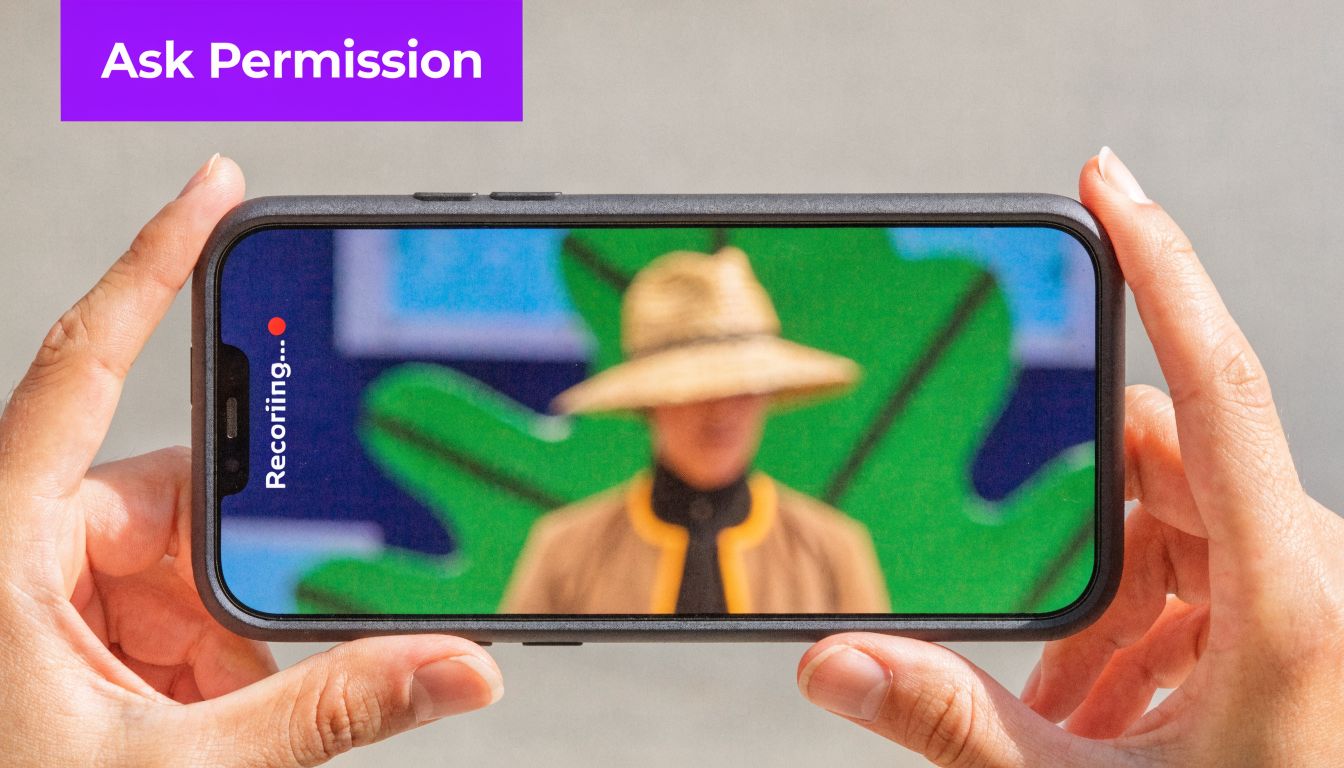 A person holding a smartphone horizontally while recording a video of someone wearing a straw hat.
