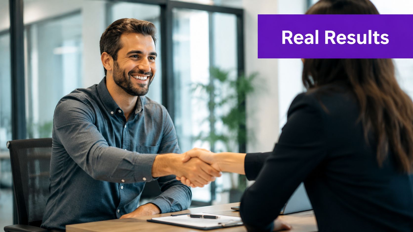 A professional man and woman shaking hands across an office desk during a business meeting.