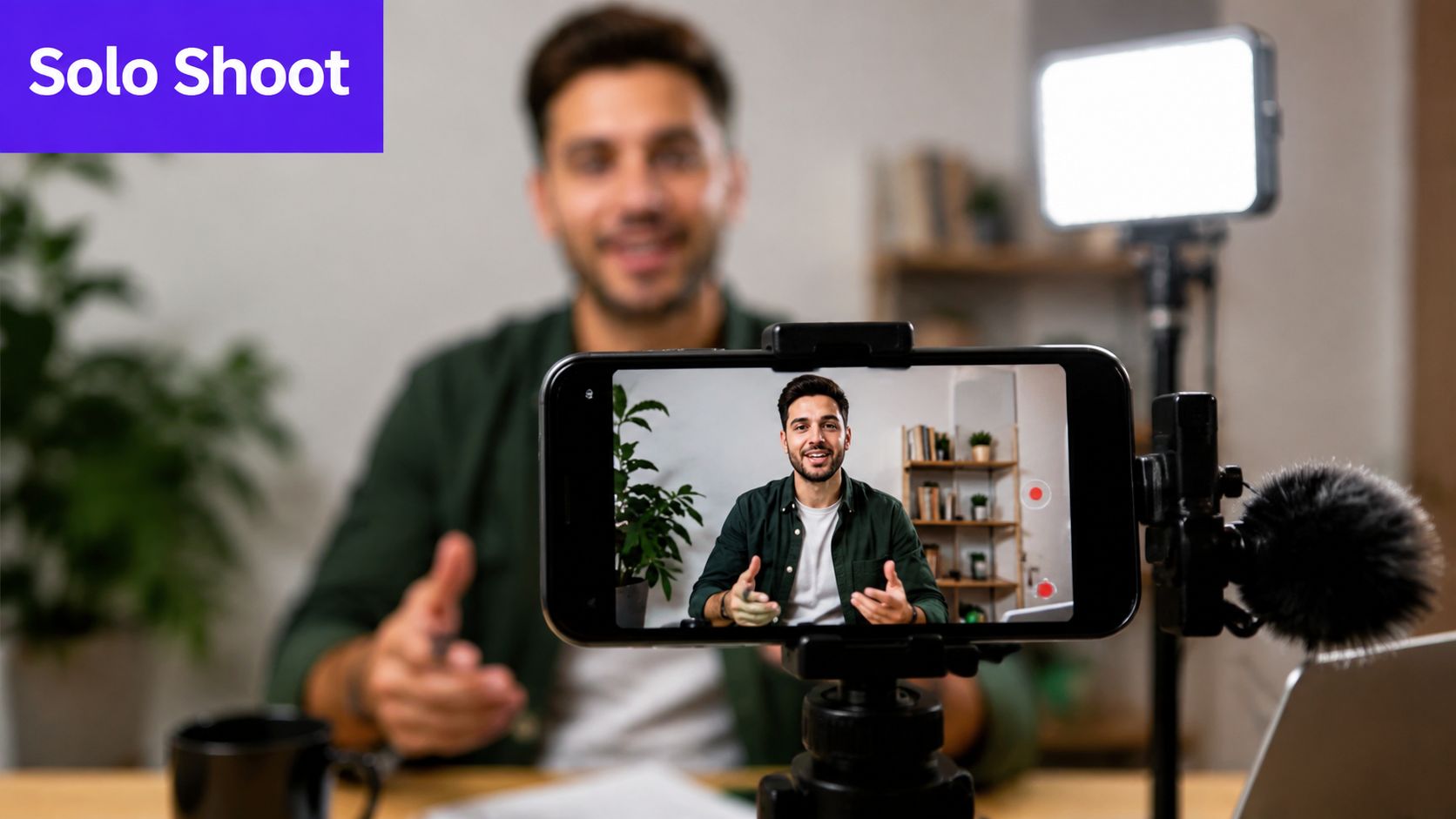 A content creator filming himself for a video blog using a smartphone, tripod, light, and microphone.