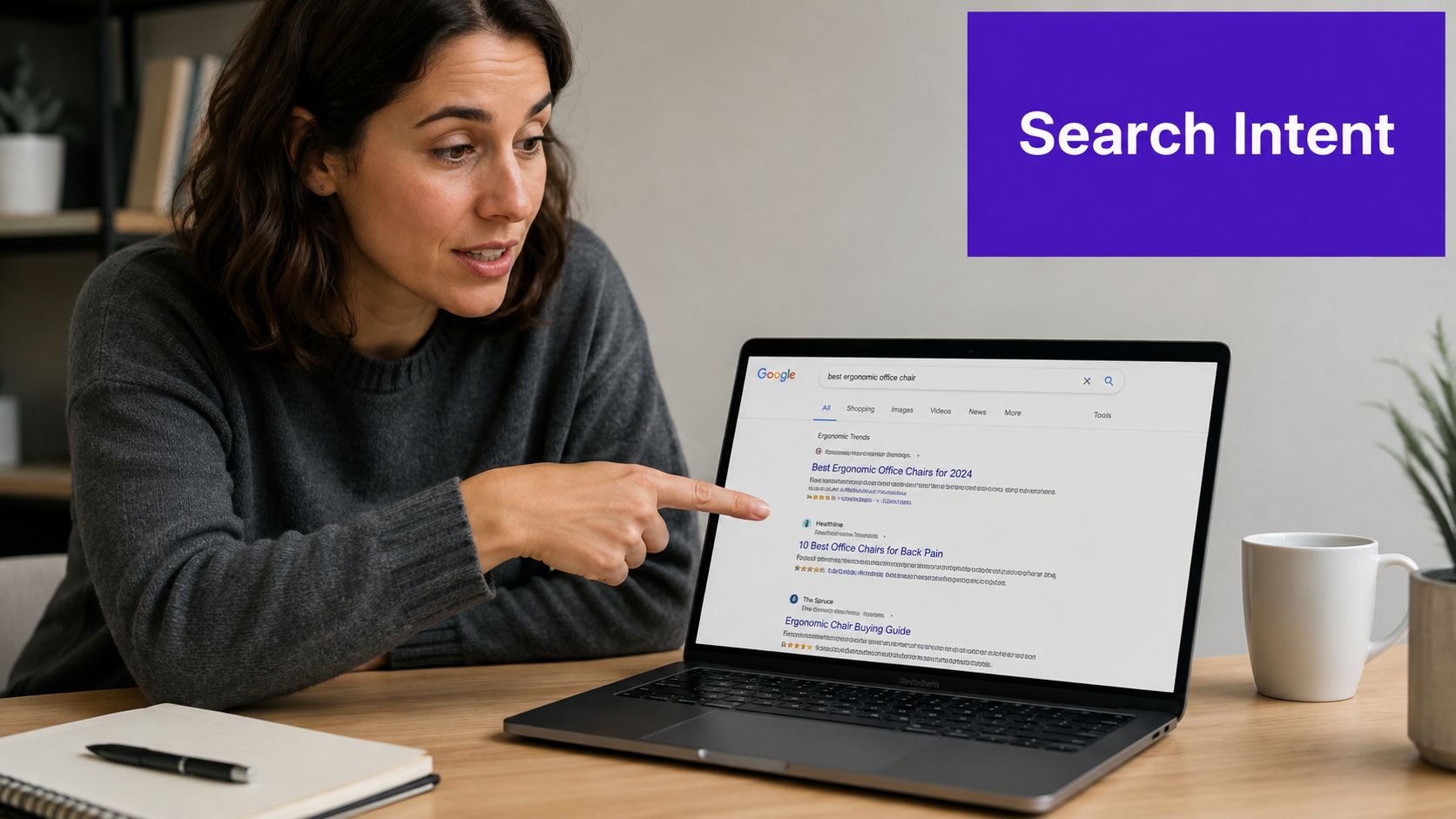 A woman pointing at a laptop screen displaying Google search results for best ergonomic office chairs.