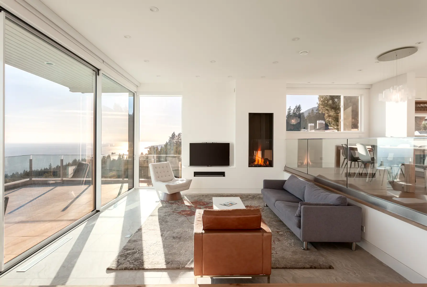 Open living area with a linear fireplace and floor-to-ceiling windows over the water, Folkstone Way rebuild in West Vancouver