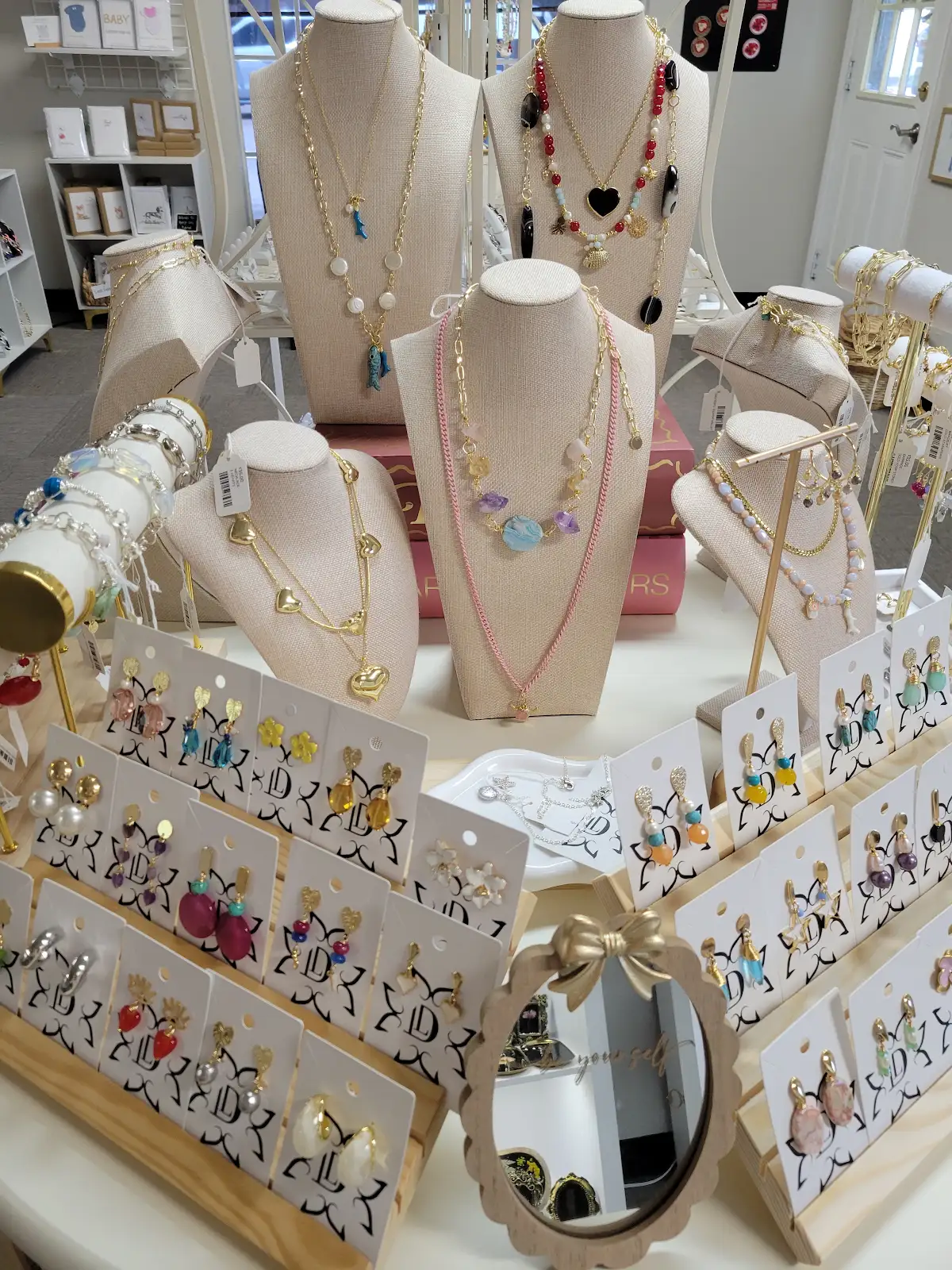 Two gold chain necklaces with heart-shaped pendants and two pairs of gold earrings on pink cards.