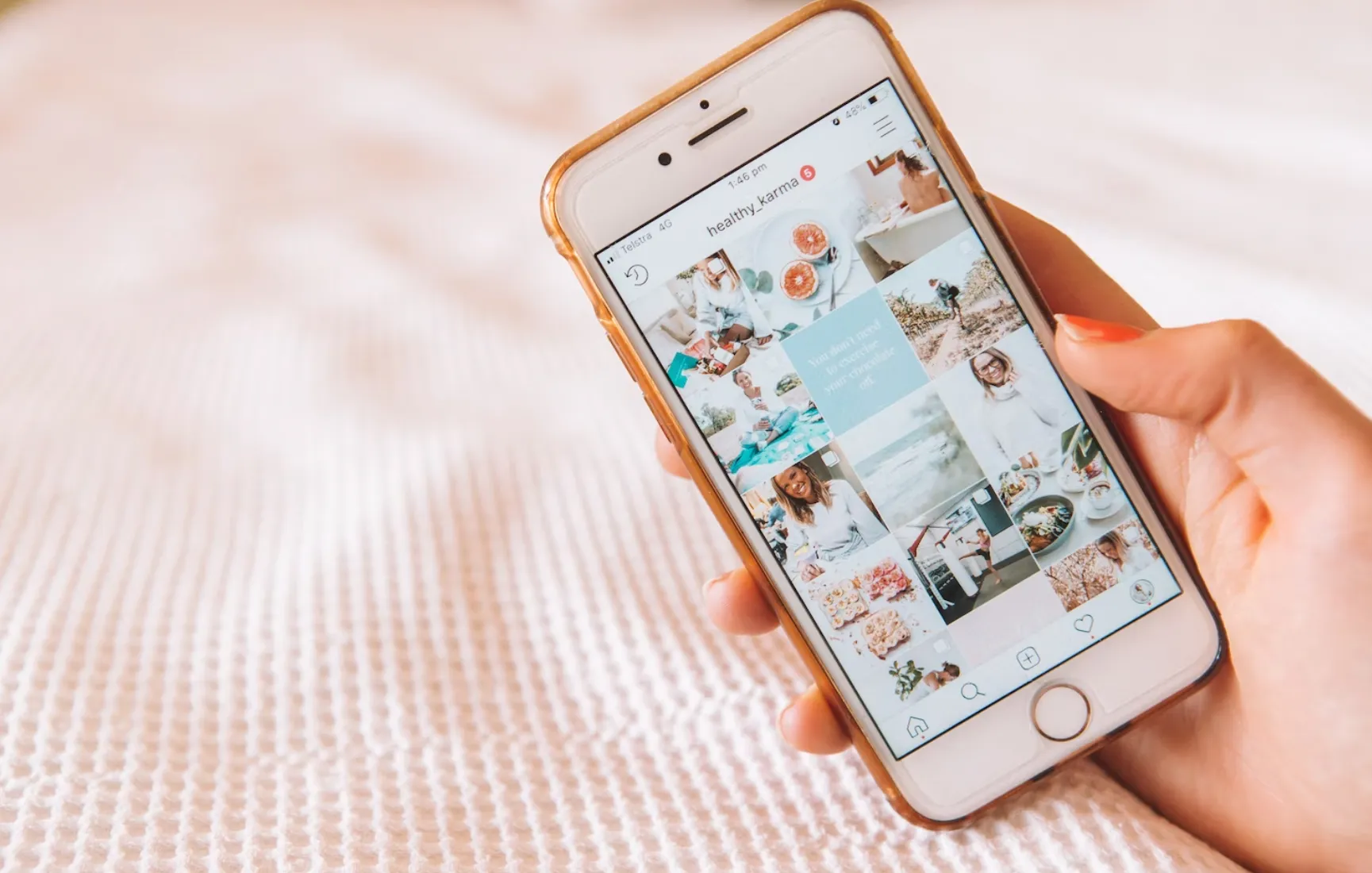 Hand holding a smart phone showing an Instagram gird, light pink background