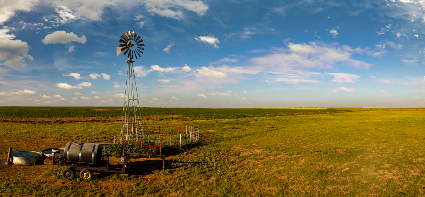 Scenic photo of a classic windmill on open farmland in West Texas. A wide rural landscape under a bright sky, perfect for showcasing Texas agriculture and countryside views.