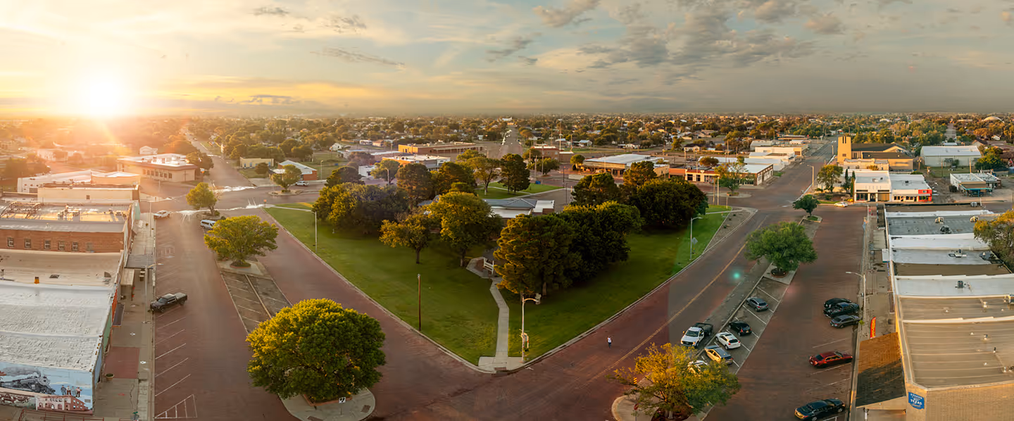 Sunrise over downtown Slaton, Texas with brick streets, historic buildings, and a central green park. A vibrant view of small-town charm and community life.