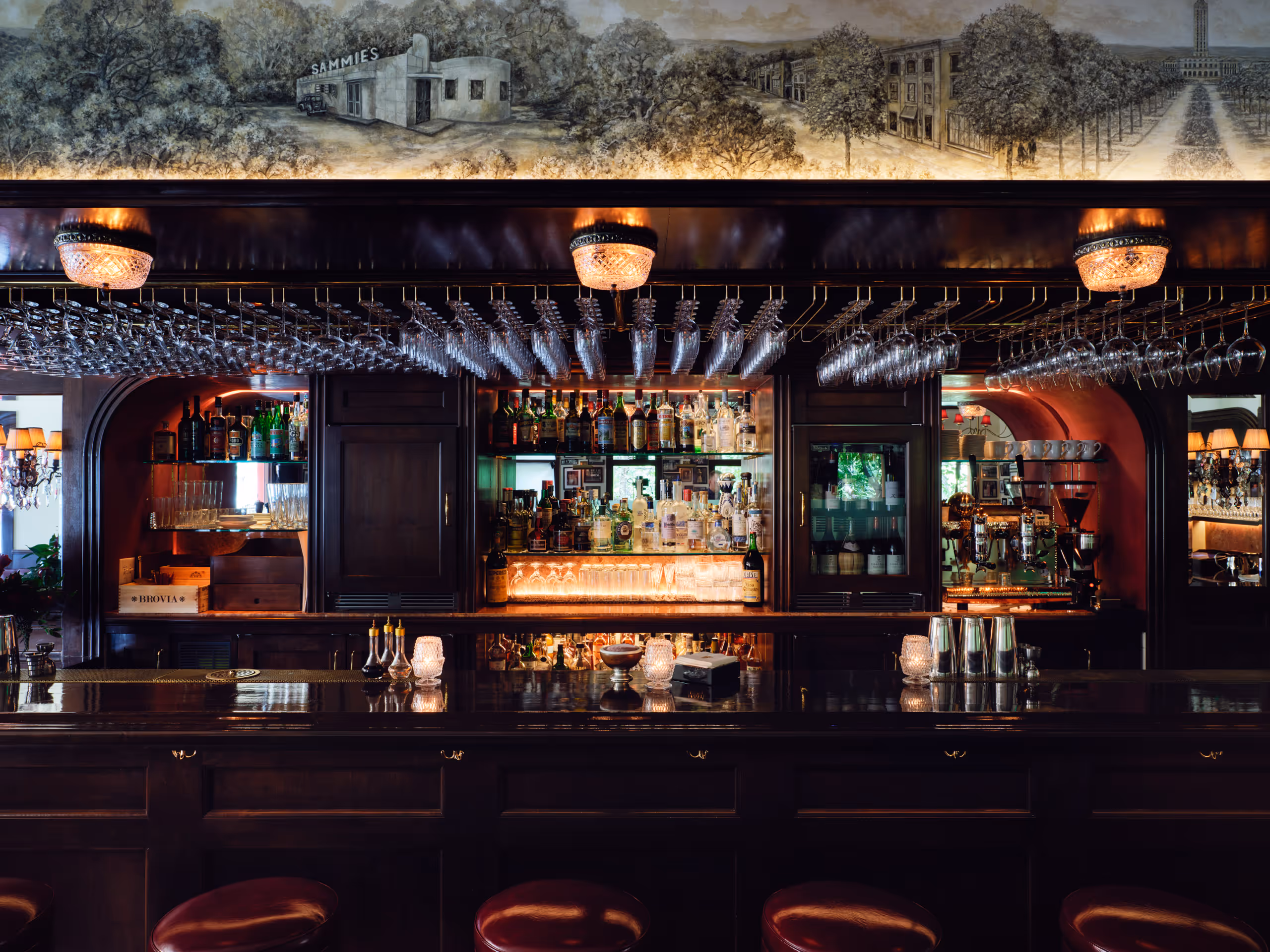 Dark wood bar with hanging wine glasses and a mural above the shelves.
