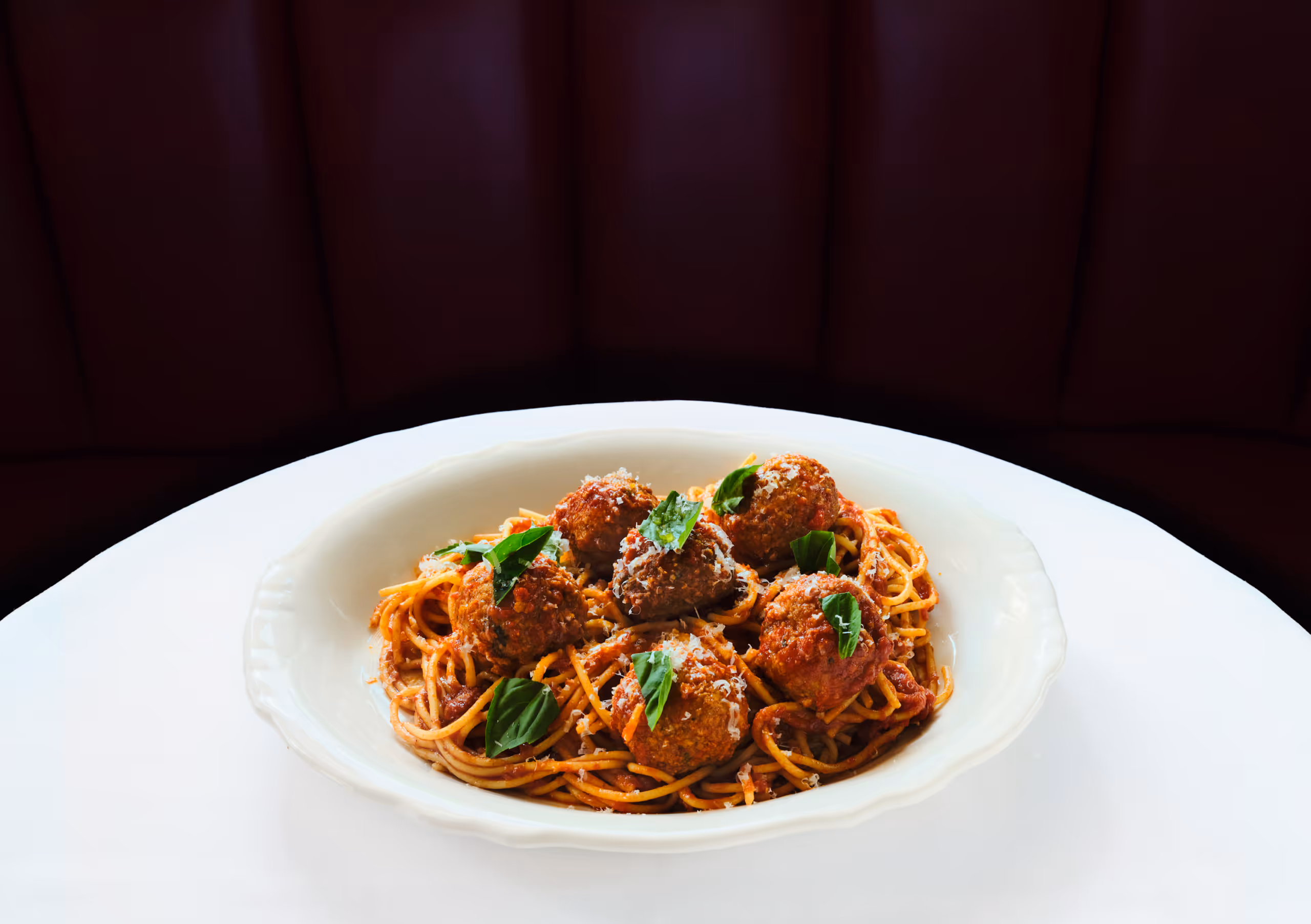Spaghetti and meatballs topped with basil on a white plate.