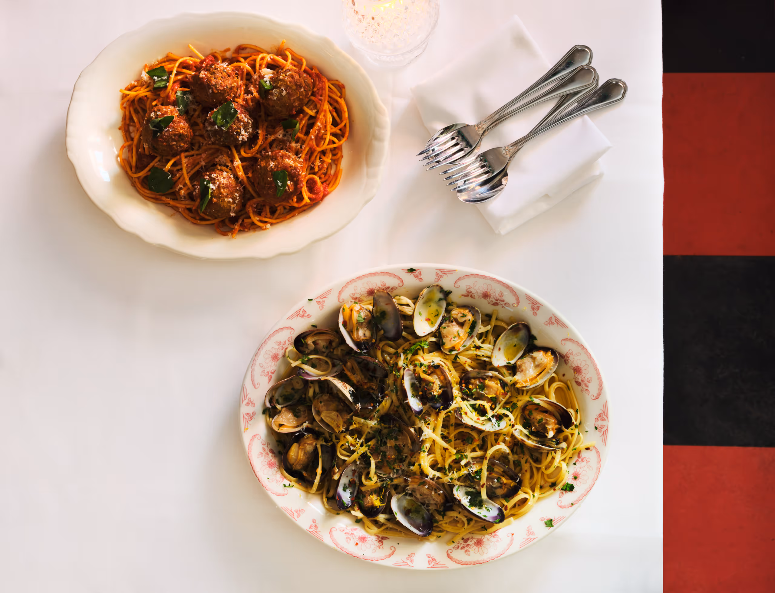 Spaghetti and meatballs beside a platter of clams on a white tablecloth.