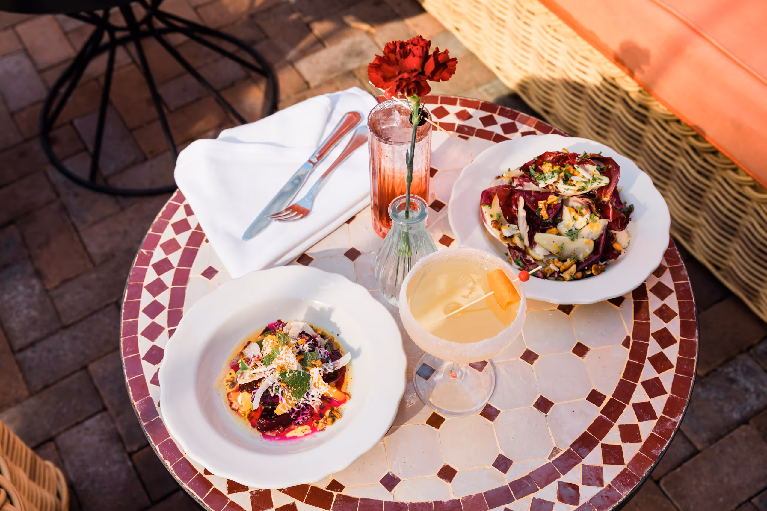 Two salads and a cocktail on a tiled outdoor table.