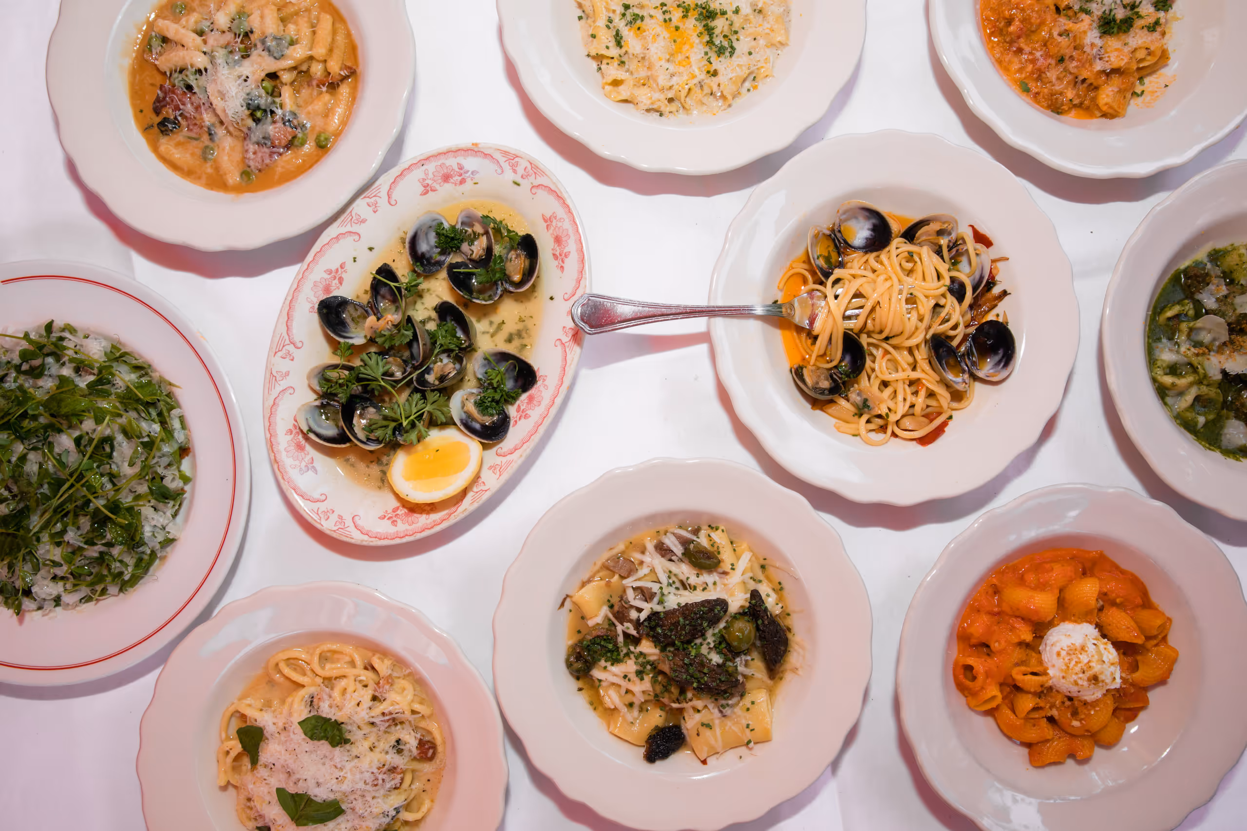 An overhead spread of pasta, clams and salad on a white tablecloth.