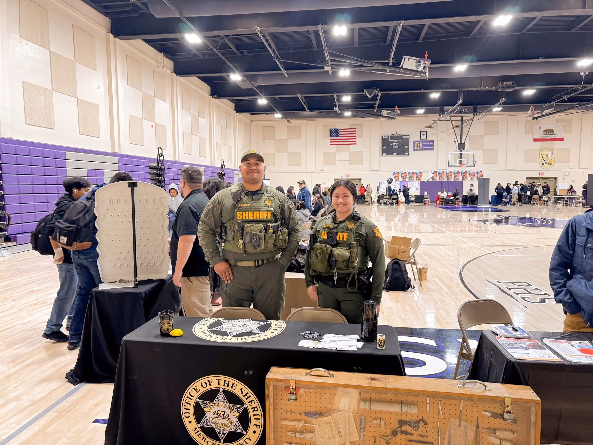 Merced County Sheriff's Deputies at a recruitment table during a community event in a school gymnasium